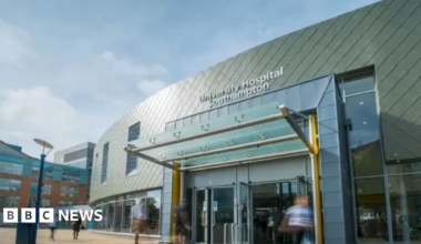 An image of Southampton Airport - it's a big building with yellow welcome shelter. Big windows on the outside. It's a sunny day with blue sky.