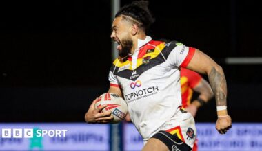 Bradford Bulls' Waqa Blake, wearing the club's home colours of white with black, yellow and red trim, runs into to score with the ball under his right arm and an expression of joy on his face