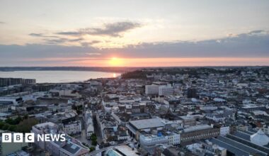A drone shot above St Helier as the sun sets into the sea beyond.