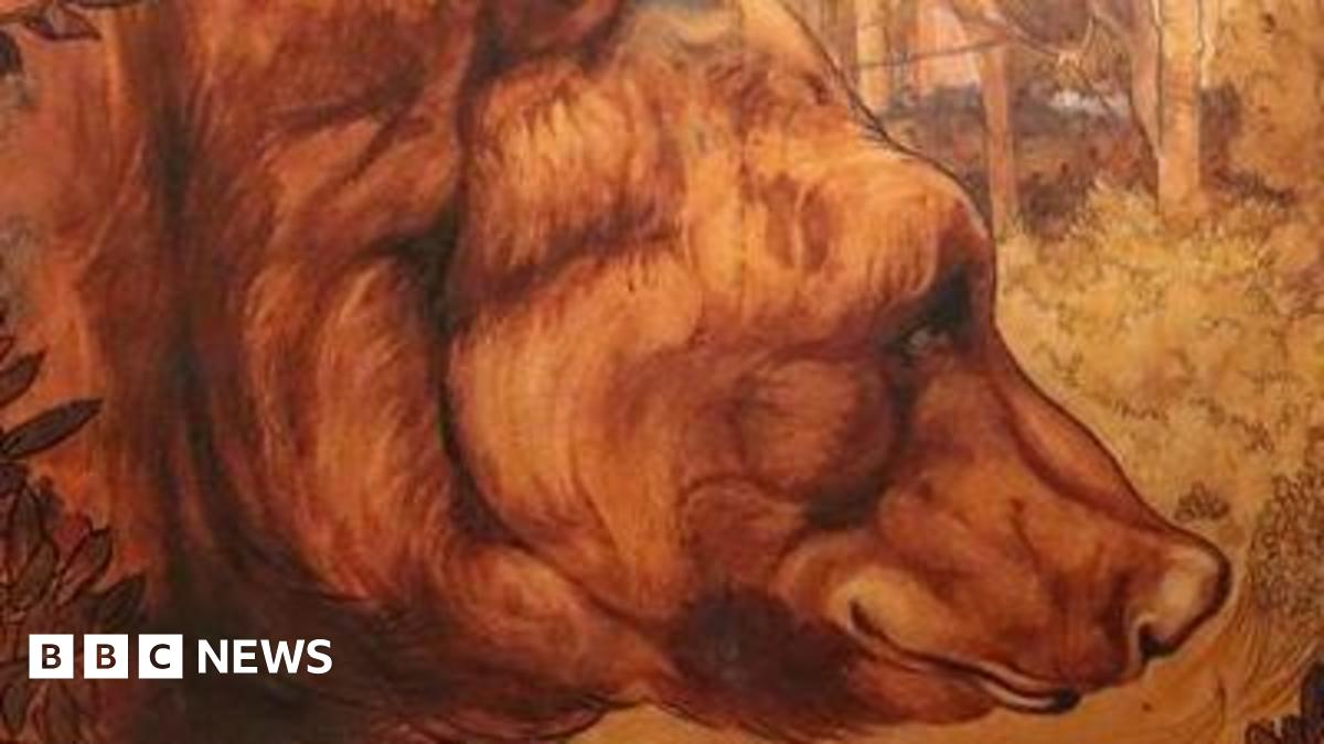 A water colour painting shows a bear in a forest with leaves in front of it. The bear's fur is brown and the forest is sunlit with the tree trunks visible. The bear fills most of the painting and looks sleepy and gentle.