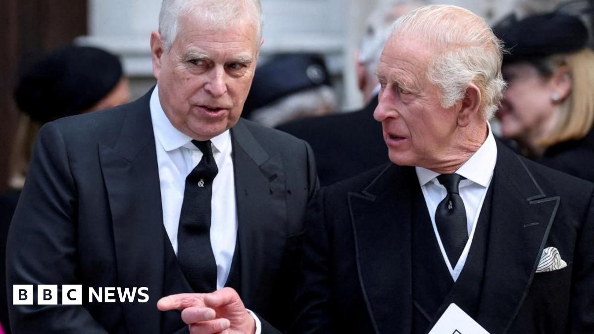 Andrew and King Charles talking as they walk. Charles points across Andrew and looks to the side while Andrew looks ahead. They both wear black suits, white shirts and black ties