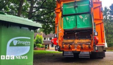 A green Shropshire Council bin in front of an orange bin lorry