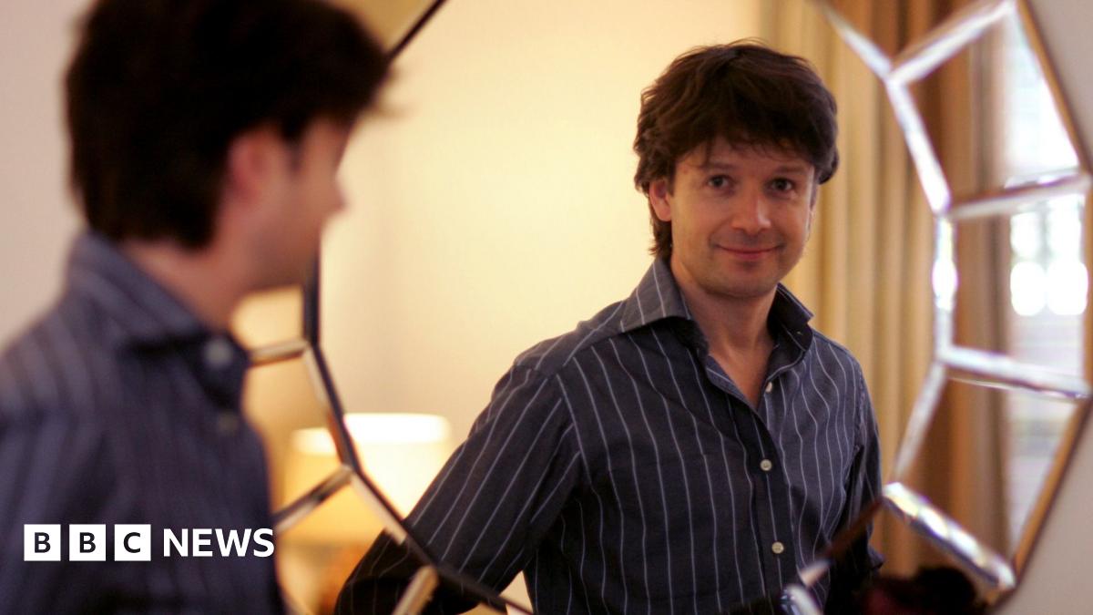A fossil of part of a crinoid that resembles a row of teeth. The markings form a curved shape with pale, tooth‑like segments set against the darker surface of the fossil. The fossil rests on another rock in the foreground.