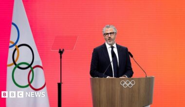 Casey Wasserman speaks to the media in Los Angeles in June 2025. He is wearing a black sweatshirt and glasses.