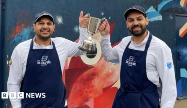 Two owners of a fish and chip shop stand outside it holding the large silver trophy.