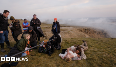 A scene of the 2026 film Wuthering Heights being shot in the Yorkshire Dales. To the left of the image are members of the crew with a boom microphone and camera. To the right Margot Robbie is lying on the ground in costume with Jacob Elordi to her side also in costume