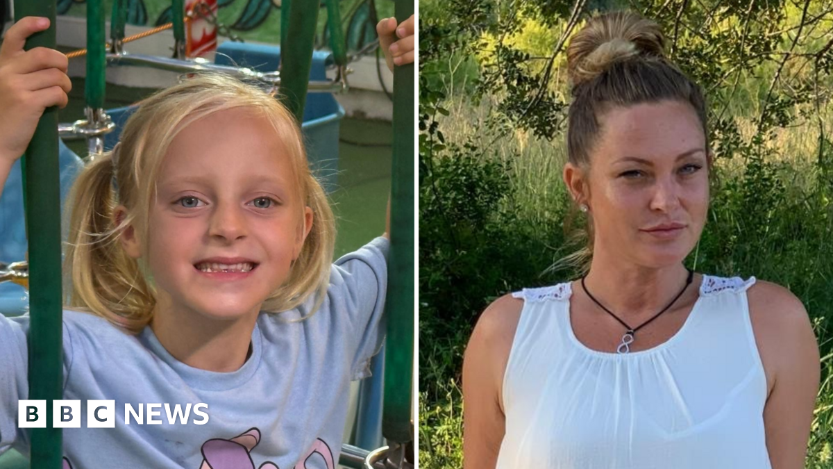 Mary Michelle Devine right in a white dress in a green outdoor area and Theia left in a play area smiling at the camera. She is a blond haired girl wearing a purple t-shirt with a cartoon character on.