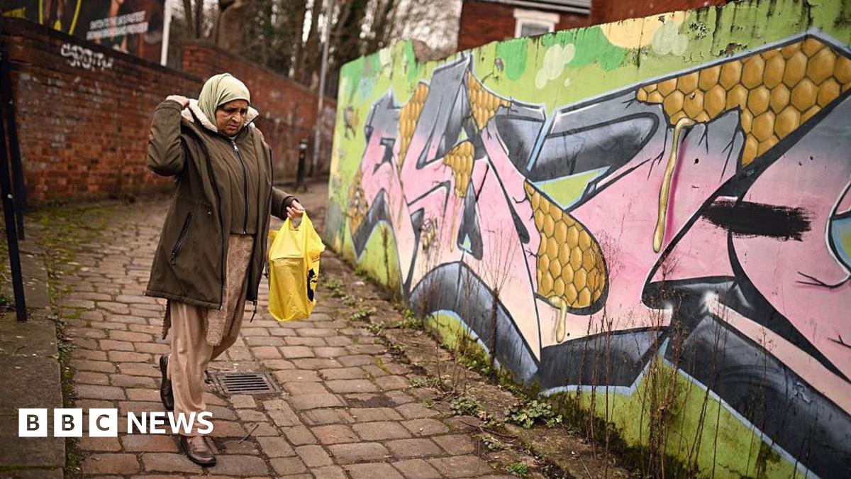 A woman passes graffiti sprayed on the wall of an alleyway in Longsight, within the Gorton and Denton parliamentary constituency