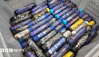 Nicola Henshaw is standing in a room where nitrous oxide canisters are being treated.  She is wearing a high-vis jacket, with a range of machines behind her in the background.