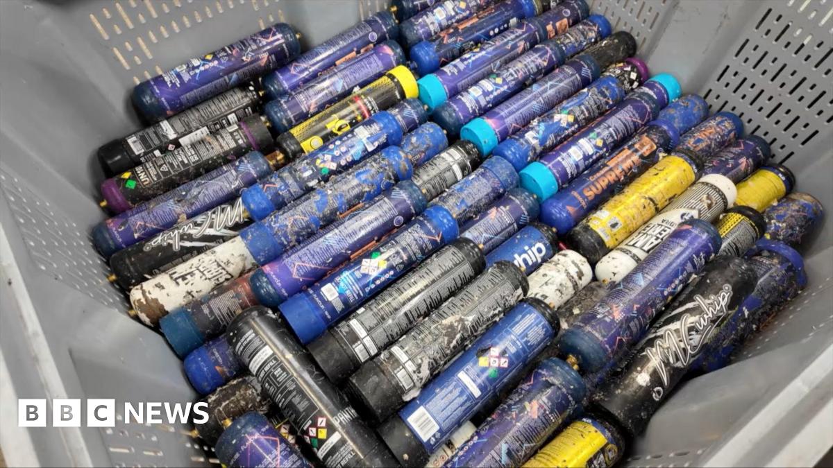 Nicola Henshaw is standing in a room where nitrous oxide canisters are being treated.  She is wearing a high-vis jacket, with a range of machines behind her in the background.