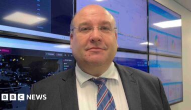Tony Moretta pictured on stage giving a talk in a darkened room. He is wearing a dark suit and glasses.