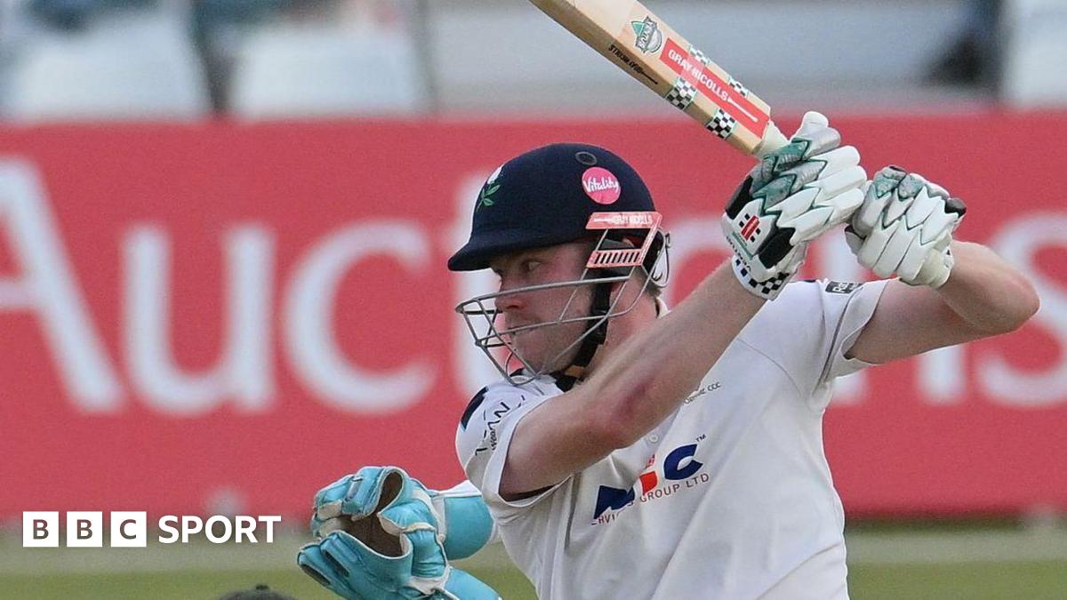 Matthew Revis batting for Yorkshire with a helmet on with wicket-keeper gloves visible behind him