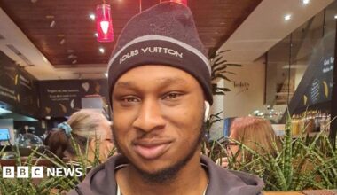 Khaleed Oladipo wearing a black hat and zip-up jacket, smiling.