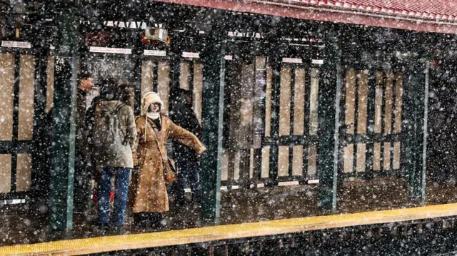 view of people standing on an outdoor subway platform as heavy snow falls