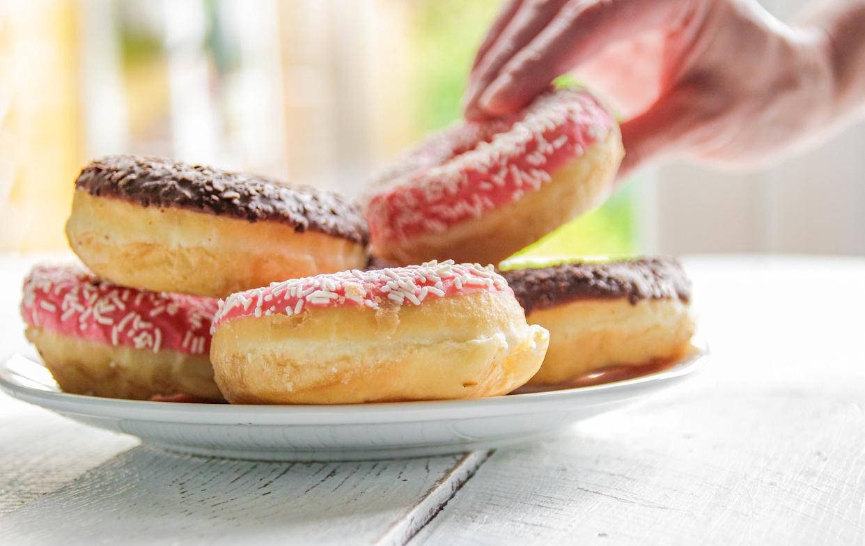 Close-up shot of a plate of doughnuts with a hand reaching in to take one.