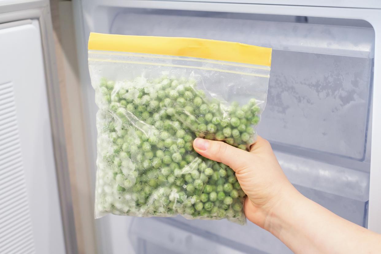 Female hand holding zip bag with a frozen green peas against open freezer background.