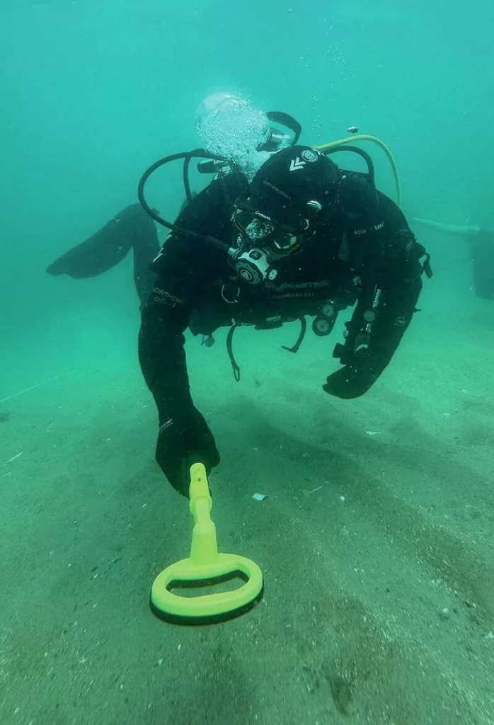 Diver using a metal detector to search for wartime artefacts on the seabed
