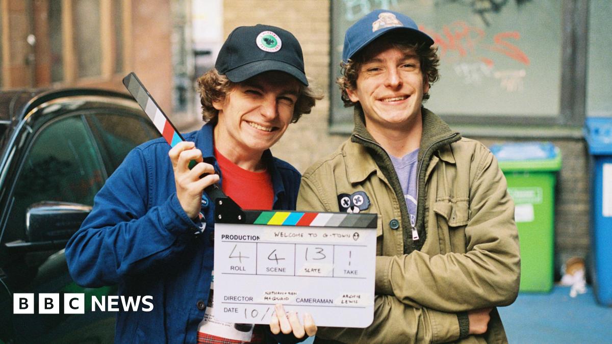 Twin brothers wearing caps smile as they pose with a movie clapperboard
