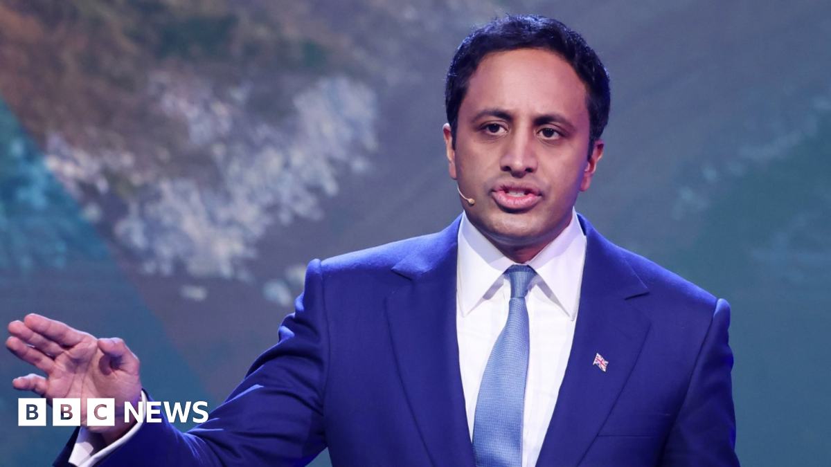 Reform UK home affairs spokesman Zia Yusuf speaks during a press conference in London. He wears a royal blue jacket with a white tie and a paler blue tie. He has short dark hair and is wearing a small union flag badge.
