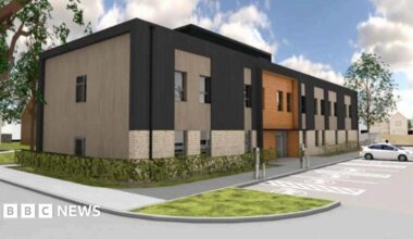 A computer-generated image of a building in Gloucester, with parking spaces positioned at the front and a car parked in one of them. The building appears to be made of black and brown material