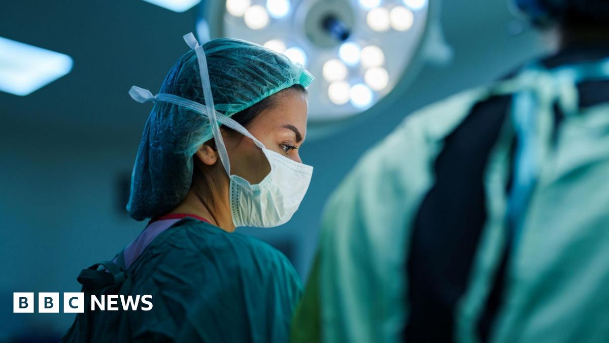 A masked female surgeon in an operating theatre