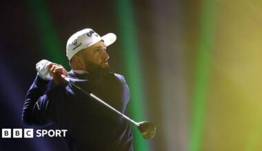Jon Rahm tees off on the 16th hole on day one of LIV Golf Riyadh. He has a black beard and is wearing a white cap, a white glove on his left hand and a navy sweater.