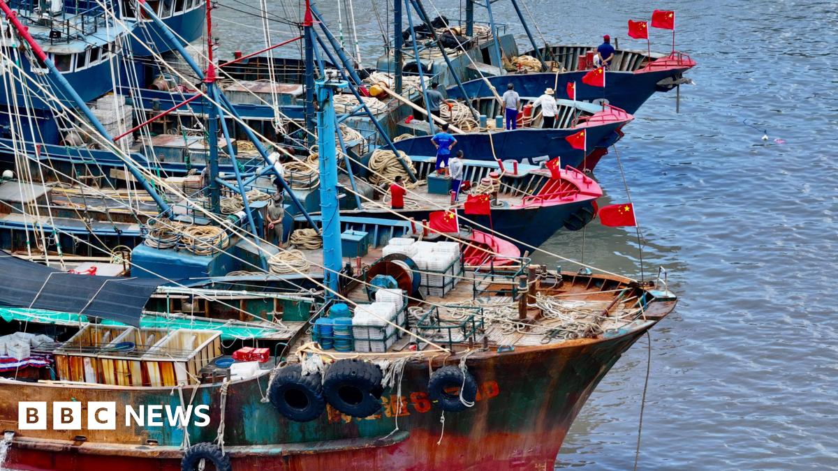 Four fishing vessels with arrays of lines and nets on their decks float in a line on calm water. They are all flying Chinese flags and three of the boats have crew standing near their bows.
