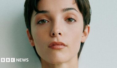 Jessica Reynolds, a woman with short, dark hair, looks to the camera with a neutral expression for a close-up photo.  She has brown eyes and is lightly made up.