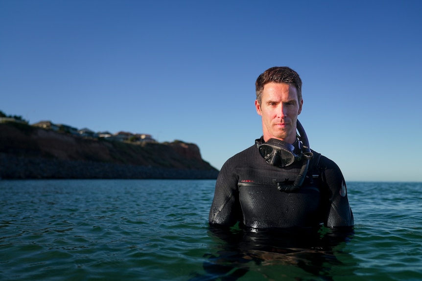 A man in a dive suit and snorkelling mask, half submerged in the water