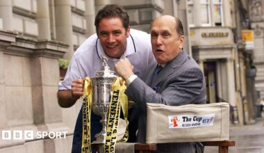 Ally McCoist and Robert Duvall hold the Scottish Cup. Duvall is in a director's chair while McCoist is leaning forward in a white T-shirt.