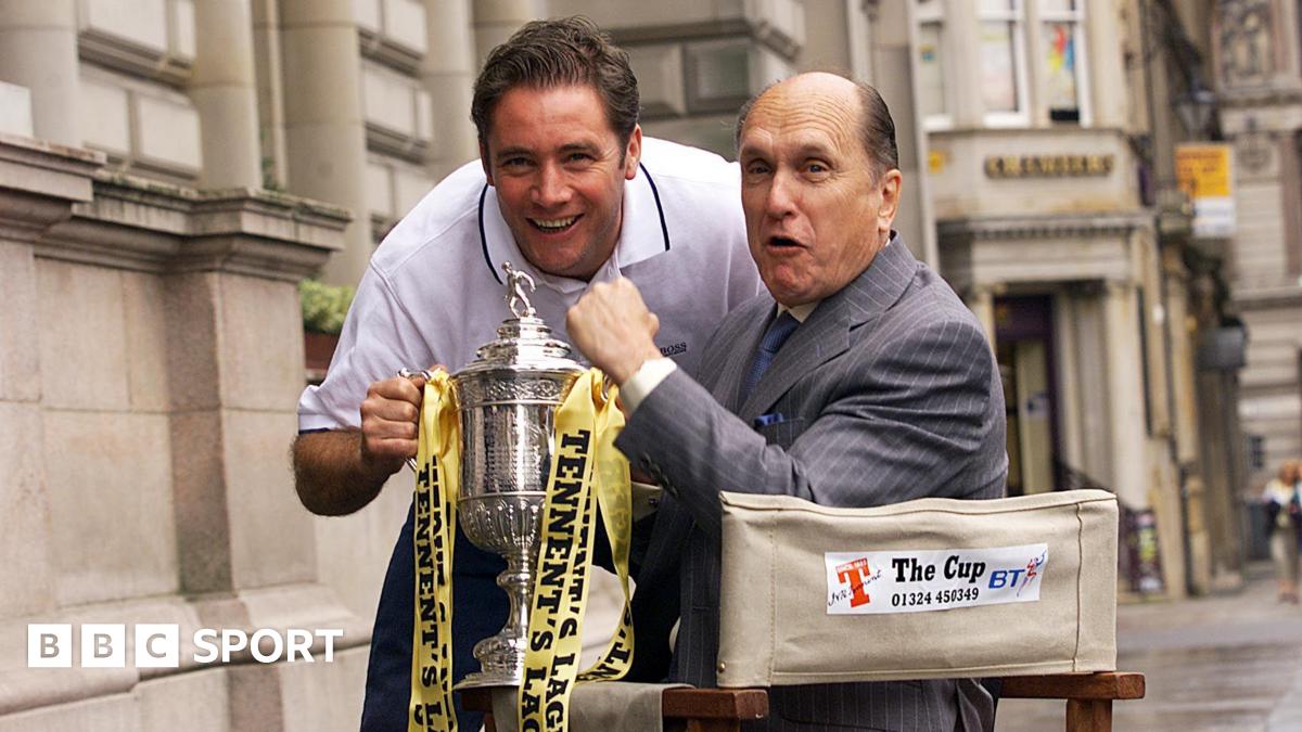 Ally McCoist and Robert Duvall hold the Scottish Cup. Duvall is in a director's chair while McCoist is leaning forward in a white T-shirt.
