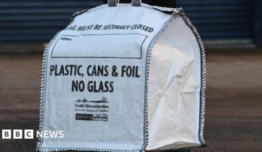 A white heavy-duty bag with "Plastic, Cans and Foil. No Glass" written on the side. In smaller words, South Gloucestershire Council is written.