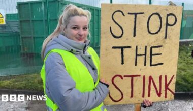 Allison Rowe who has short greying hair with pursed lips and wearing maroon rimmed round glasses and a denim top