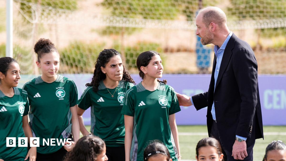 Prince William talks to a group of young girls in green football kits.