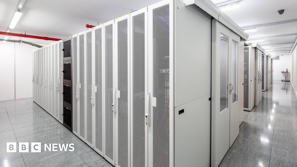 A corridor of white, mesh‑fronted server racks in a brightly lit data centre.