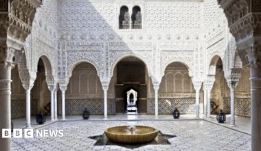 A courtyard with tiled floor, fountain and white ornately carved walls