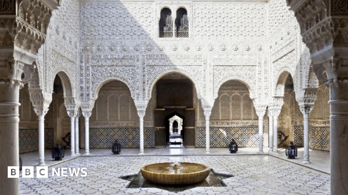 A courtyard with tiled floor, fountain and white ornately carved walls