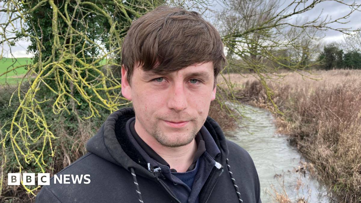 Connor Bryan, who has brown hair and is wearing a black hooded top, stands in front of a river.