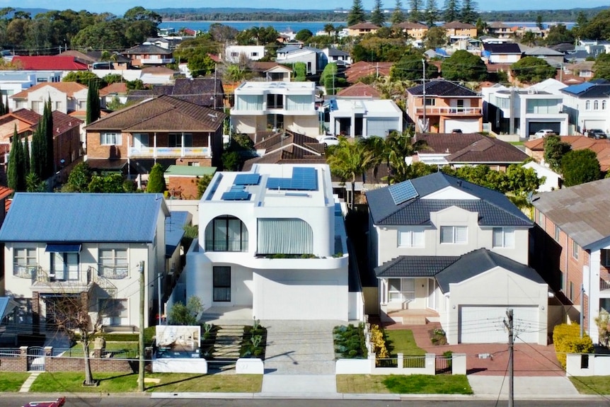An overhead shot of expensive looking houses in an estate near the beach, with the ocean seen in the background.