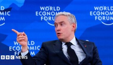 François-Philippe Champagne in navy suit and tie points his right hand towards the right with the blue backdrop that reads "World Economic Forum"