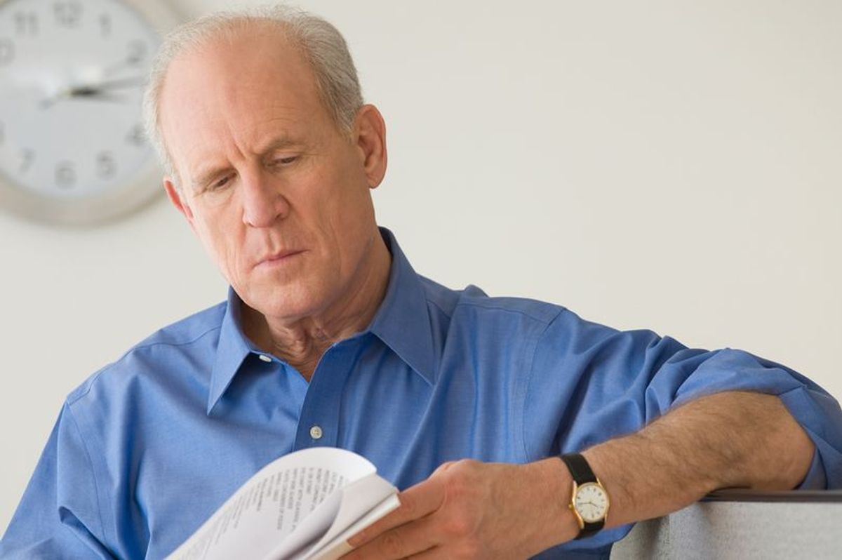 A senior man is reading a document with a pensive expression on his face 