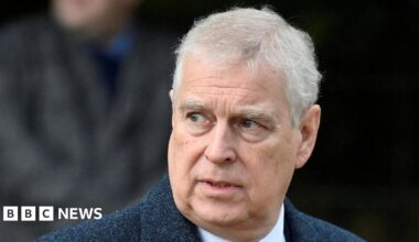 Headshot of Andrew who looks off to the side with his mouth slightly open. The background is blurry but it appears there's a person walking behind him. Taken in December 2022