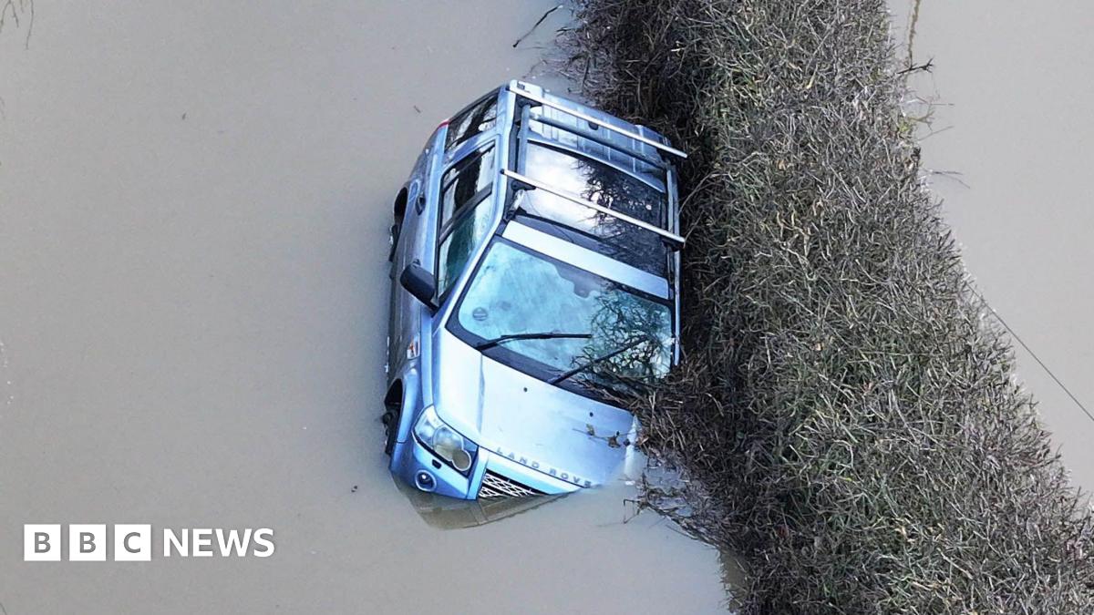 A silver Land Rover stuck in flood water. It is slightly tipped to the side and water is coming up over one of its headlights.