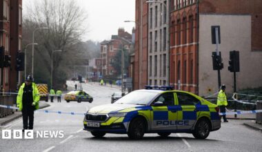 Two officers stand with their backs to the camera next to police tape with a police car in the road in the background in Leicester city centre on Wednesday morning.
