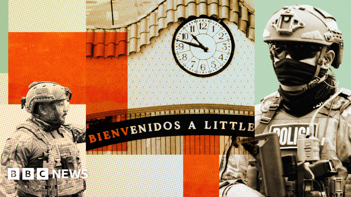 A man carries a box of groceries while crossing a street in a neighbourhood with many business signs in Spanish