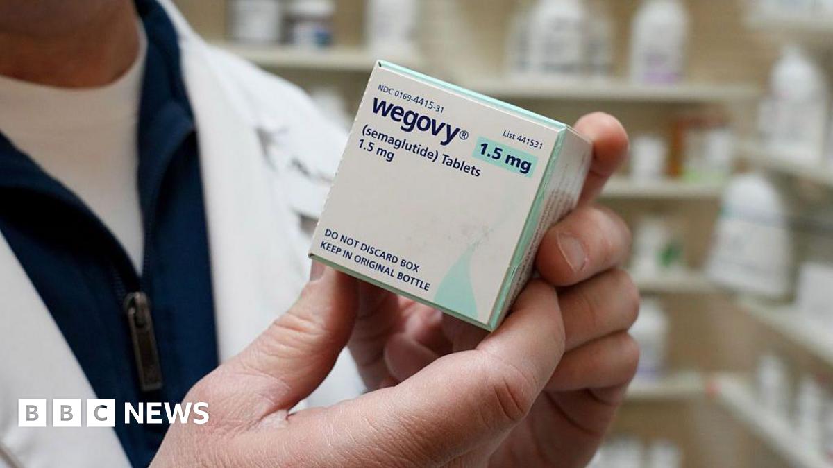 A close-up of a pharmacist holding a box of Wegovy weight-loss pills in a pharmacy