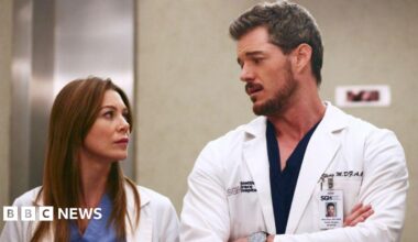 Eric Dane and Ellen Pompeo in a still from Grey's Anatomy. Both wear white medical coats over light blue and black scrubs.
