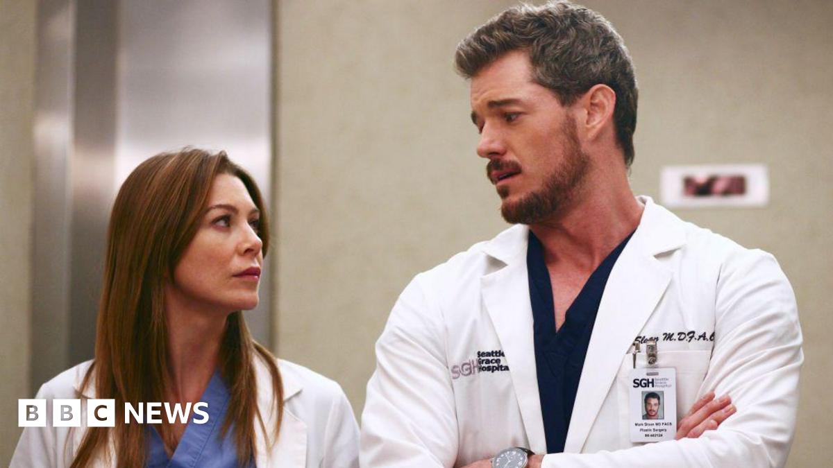 Eric Dane and Ellen Pompeo in a still from Grey's Anatomy. Both wear white medical coats over light blue and black scrubs.