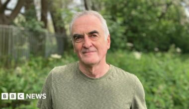 Ash Smith looking at the camera - he's got white hair, black eyebrows and is wearing a green T-shirt. He's white.