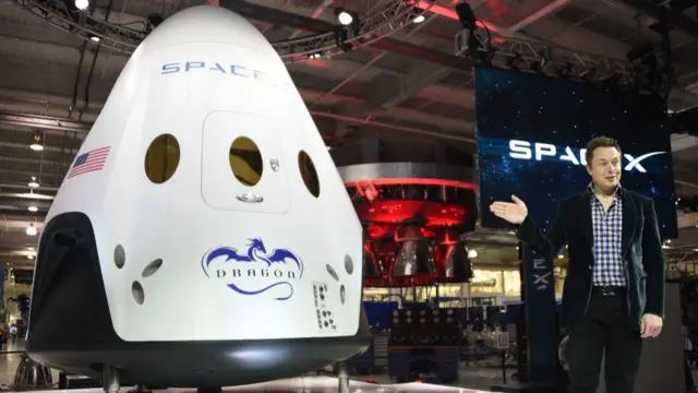 Elon Musk unveils Dragon at an event in 2014 - its a large capsulte, mostly white, with a US flag on the side and a picture of a dragon. It's eight metres tall, and about four metres wide